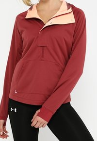 Giacca pullover rossa con cappuccio rosa chiaro, dotata di tasca frontale e chiusura con zip. Realizzata in tessuto morbido e progettata con maniche lunghe.