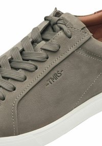 Grå lädersneakers med teksturerad yta, stickade detaljer, runda snören och en vit gummisula med inpräntat varumärkeslogotyp.