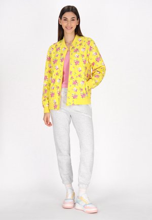 Geel bomberjack met een roze bloemenpatroon, gecombineerd met een roze top en grijze sweatpants. Schoeisel heeft pastelkleuren en een chunky ontwerp.