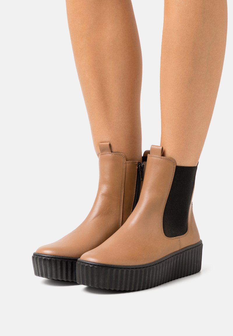 Brown leather ankle boots with a black elastic side panel, round toe, and a textured black platform sole. Zipper detail on the side.