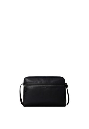 Borsa a tracolla nera Calvin Klein con texture traforata, tasca frontale con zip e tracolla regolabile su sfondo bianco.