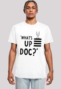 Tricou alb din bumbac cu un design grafic care include textul "CE MAI FACI, DOC?" și un iepure de desene animate care răsare deasupra unei secțiuni cu dungi.