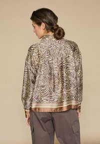 Brun satin bomberjakke med zebra mønster, med kontrasterende brun satinkant og manchetter samt en afslappet pasform.