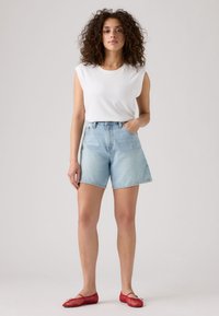 Lichtgewassen denimshorts met een losse pasvorm, gecombineerd met een effen witte mouwloze top en rode platte schoenen. Gladde textuur en casual ontwerp.
