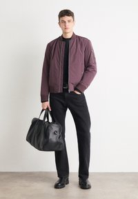 Burgundy bomber jacket with zip closure, black knit shirt, black jeans, and black leather duffel bag, worn with black boots.