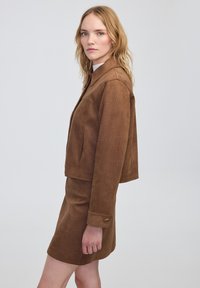 Chaqueta recortada de textura marrón con cuello de solapa y mangas largas, combinada con una falda a juego, ambas con patrones sutiles.