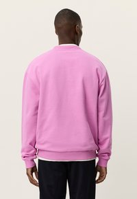 Ροζ φούτερ με στρογγυλή λαιμόκοψη, μακριά μανίκια και ριμπ μανσέτες. Το ύφασμα φαίνεται μαλακό με άνετη εφαρμογή και ομαλή υφή.