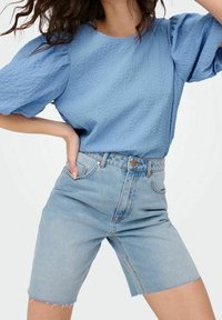 Top azzurro chiaro texturizzato con maniche a palloncino abbinato a pantaloni corti di jeans chiari a vita alta, caratterizzati da orlo grezzo e design a cinque tasche classiche.