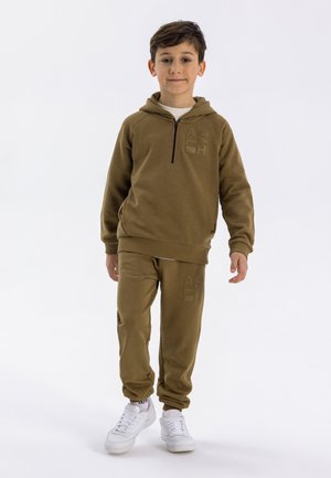 Khaki hooded tracksuit with a zip, featuring embossed logo details. Made of soft material, paired with white sneakers for contrast.