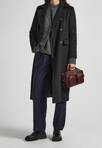 Abrigo de lana negro con diseño cruzado, suéter gris de punto, pantalones azules marino a rayas y un pequeño bolso de cuero burdeos. Zapatos negros.