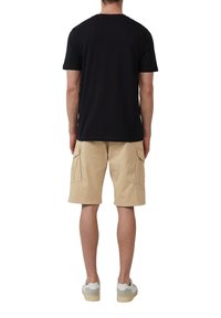 Schwarzes Baumwoll-T-Shirt mit Rundhalsausschnitt, kombiniert mit beigen Cargo-Shorts mit Seitentaschen, abgerundet mit weißen und grauen Sneakers.