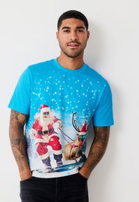 Modré tričko s krátkým rukávem s barevným motivem Santa Clause a soba, s vločkami sněhu a zimním pozadím.