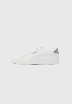 Baskets blanches en cuir synthétique, avec une texture lisse, un design à lacets, un accent de talon violet clair et un logo bien visible.