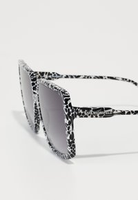 Black and white patterned sunglasses with a rectangular shape, wide frames, and gradient lenses. Features logo on the temple.