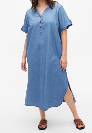 Spijkerjurk in lichtblauw, V-hals met knoopdetails, opgerolde korte mouwen, zijsplitten en een losse pasvorm. Platte, bruine sandalen inbegrepen.