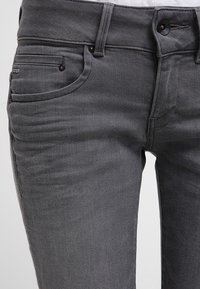 Grå denimjeans med en figurnära design, som har en knappstängning, framfickor och en slät yta. Diskret sömdekoration vid sömmarna.