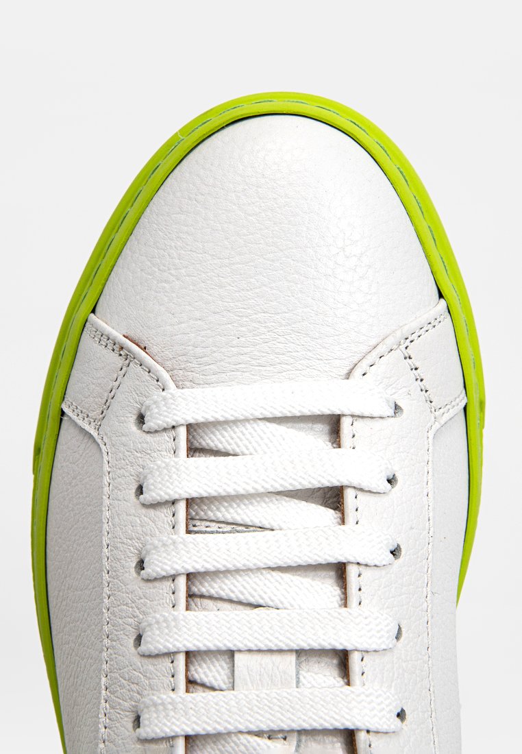 Weiße Ledersneaker mit strukturiertem Finish, ausgestattet mit einer leuchtend grünen Gummisohle und weißen Schnürsenkeln, mit Fokus auf der Zehenkappe und dem oberen Teil.