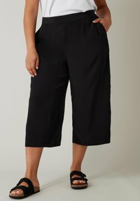 Zwarte culottes van lichtgewicht stof, met een gladde textuur, zijzakken en een relaxte pasvorm, eindigend op de kuit.