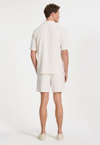 Polo shirt pour hommes en crème, à manches courtes et shorts assortis ; texture douce et coupe décontractée, avec un col et sans motifs ou accents visibles.