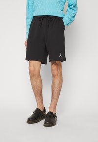 Black cotton shorts with an elastic waistband and drawstring, featuring a small white logo on the lower left leg.
