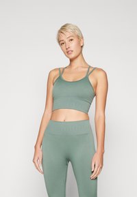 Crop top vert côtelé avec des bretelles fines, associé à un legging taille haute assorti. Texture lisse et design ajusté pour le confort.