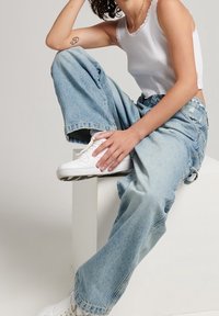 Jeans de mezclilla de pierna ancha en azul claro combinados con una camiseta sin mangas blanca, con escote festoneado y llevados con zapatillas blancas.