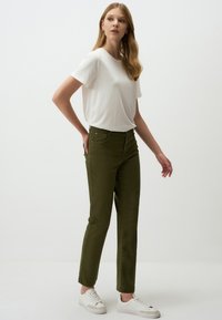 Olijfgroene katoenen broek met een aansluitend ontwerp en vijf zakken, gecombineerd met een losse witte t-shirt en witte sneakers.