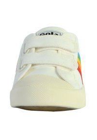 Zapatilla de lona blanca con dos tiras de Velcro, que presenta una franja de arcoíris multicolor en el lado y una suela de goma texturizada.