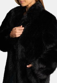 Cappotto in pelliccia sintetica nera con colletto alto, caratterizzato da una texture morbida, tasche laterali e una vestibilità comoda, messo in risalto da una finitura lucida.