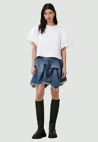 White puff-sleeve crop top, denim mini skirt with layered ruffles and frayed edges, paired with knee-high black boots.