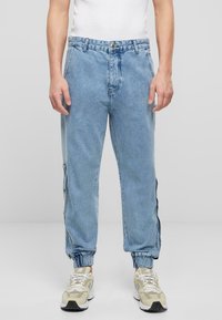 Pantaloni jogger din denim de culoare albastru deschis, cu croială relaxată, manșete elastice, nasturi pe lateral și un design clasic cu cinci buzunare.