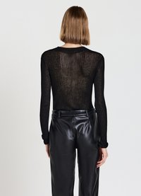 Maglietta nera a maniche lunghe in tessuto a costine trasparenti, abbinata a pantaloni in pelle nera a vita alta. Scollo sottile e polsini aderenti.