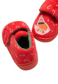Zapatillas de forro polar rojo con estampado de bastones de caramelo, forro verde y cara de duende bordada en un lateral. Correa de velcro para fácil uso.