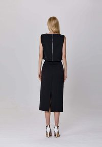 Robe noire avec un dos haut, sans manches, à silhouette droite, mi-longue, dotée d'une fermeture éclair arrière et d'une fente latérale. Associée à des escarpins noirs et blancs.