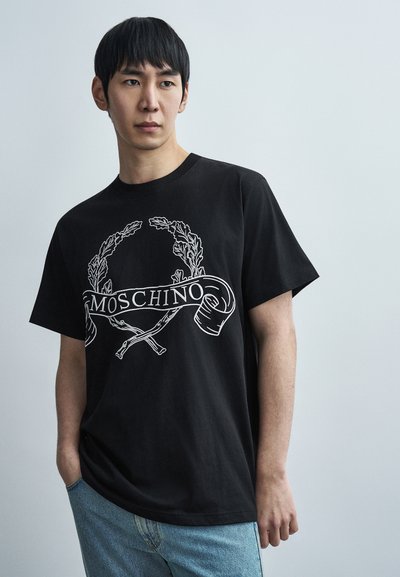 Μαύρο βαμβακερό T-shirt με λευκό γραφικό σχέδιο που απεικονίζει στεφάνι δάφνης και τη λέξη "MOSCHINO" σε ένα κυρτό κορδέλα, με άνετη εφαρμογή.