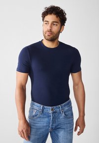 Marineblå kortermet t-skjorte laget av bomull, med rund halsdesign. Bæres med lyseblå denimjeans. Enkel og tettsittende silhuett.