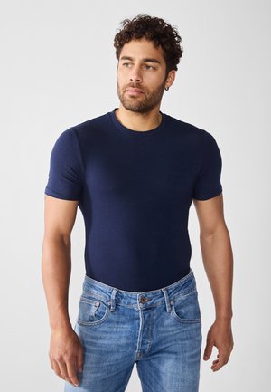 T-shirt navy a maniche corte in cotone, con scollo a girocollo. Indossato con jeans in denim azzurro chiaro. Silhouette semplice e attillata.