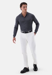 Dunkelgraues langärmeliges Polohemd, weiße Hose und schwarze Schuhe. Das Outfit verfügt über einen Knopfkragen und einen schwarzen Gürtel. Strukturierter Stoff.