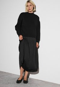 Black sweatshirt with a high neckline, relaxed fit. Pleated black midi skirt with asymmetrical hem and a smooth texture. Glittery black flats.
