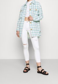 Jasnoniebieska kraciasta koszula-ramoneska z złotymi guzikami, biały krótki top, białe dżinsy z przetarciami i czarne sandały na paskach.