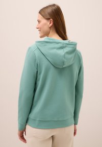 Felpa verde menta con una vestibilità rilassata, caratterizzata da un grande cappuccio, polsini a coste e una texture liscia e morbida. La vista posteriore mostra il design senza dettagli.