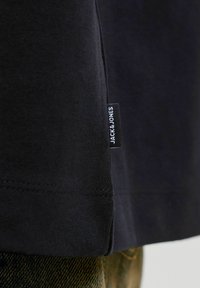 Črno bombažno majico s pravim robom, stranskim razporkom in diskretno blagovno oznako. Gladek tekstura z natančnimi šivi.