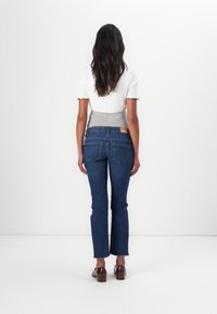 Modré džíny s rozšířenými nohavicemi a surovým lemem, kombinované s přiléhavým bílým topem se šedým žebrovaným pasem a vlnitými rukávy. Hnědé obuv.