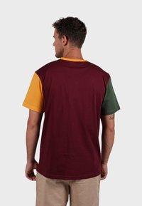 T-shirt à manches courtes en plusieurs couleurs, avec des sections bordeaux, moutarde et verte. Fabriqué en coton doux, avec une coupe décontractée et col rond.