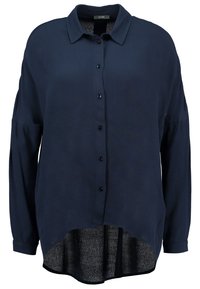 Marinblå blus i ett lätt tyg, med knappstängning fram, långa ärmar och en längre bakdel med en rundad form.