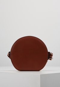 Borsa a tracolla rotonda in pelle marrone con texture liscia e dettagli di cucitura visibili, dotata di una tracolla regolabile e un design minimalista.