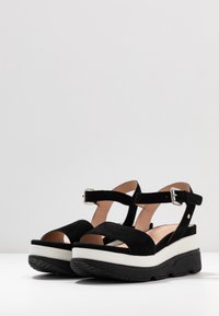 Sandali neri in suede con cinturini regolabili alla caviglia, design open-toe e suole in plateau bianche chunky con fondi in gomma nera testurizzata.