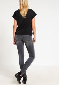 Camisa negra de manga corta combinada con jeans ajustados grises, que presentan una textura suave y sutiles detalles en los bolsillos traseros. Zapatos negros completan el conjunto.