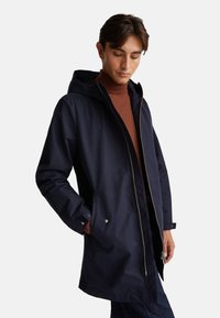 Granatowa wodoodporna kurtka z kapturem, przednim zamkiem błyskawicznym i mankietami zapinanymi na napy. Posiada dwie boczne kieszenie i minimalistyczny design.