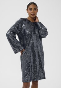 Langsleeve grijs jurk bedekt met pailletten, met een ronde halslijn en twee zijzakken. De stof is glanzend en reflecterend.